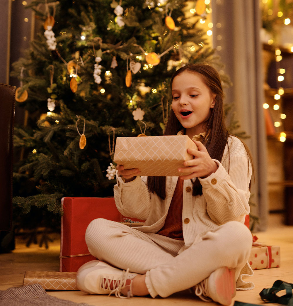 Tüdruk naudib jõulupuu all kingitust.