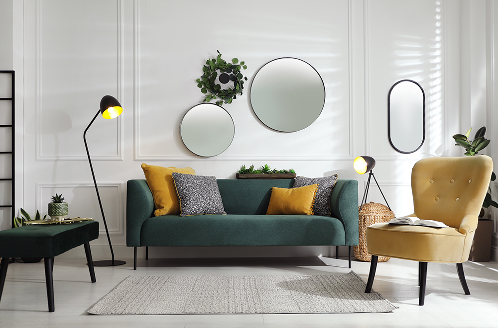 Kaasaegne elutuba heledates toonides, rohelise diivani, kollaste patjade ja ümmarguste peeglitega seinal.