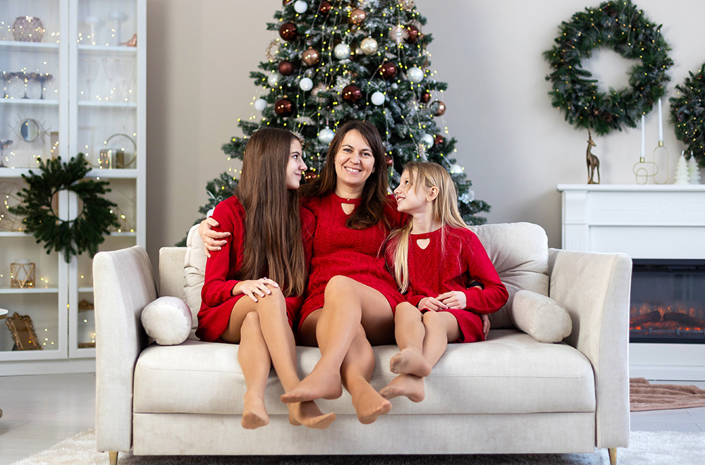 Ema ja tema tütred punastes kleitides veedavad jõuluaega koos kuuse juures.