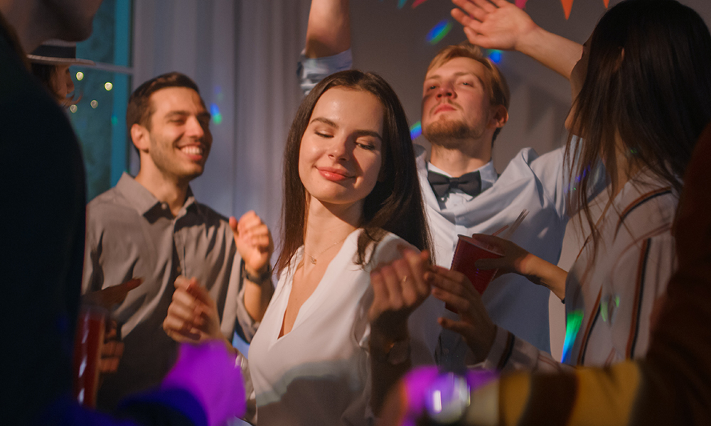 Grupp inimesi, kes tantsivad peol, sealhulgas naine, kes naudib muusikat.